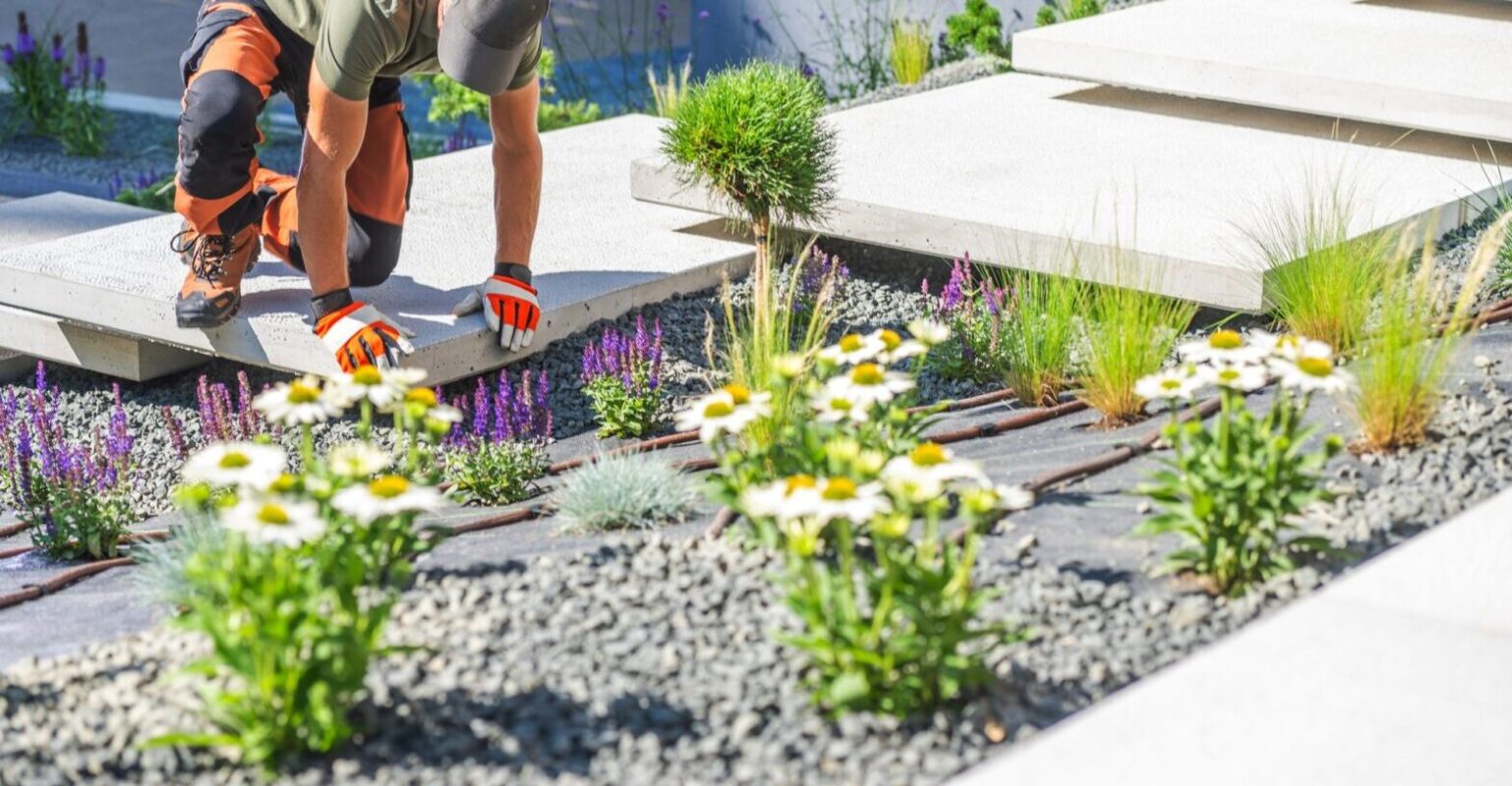 Gardener Planting Flowers in a Modern Landscape Design on a Sunny Day With Stone Pathways